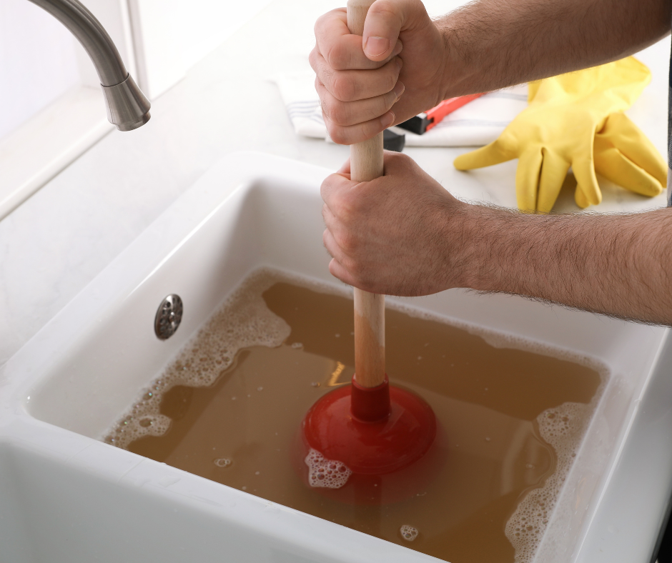 A sink that is clogged with brown water is being plunged 